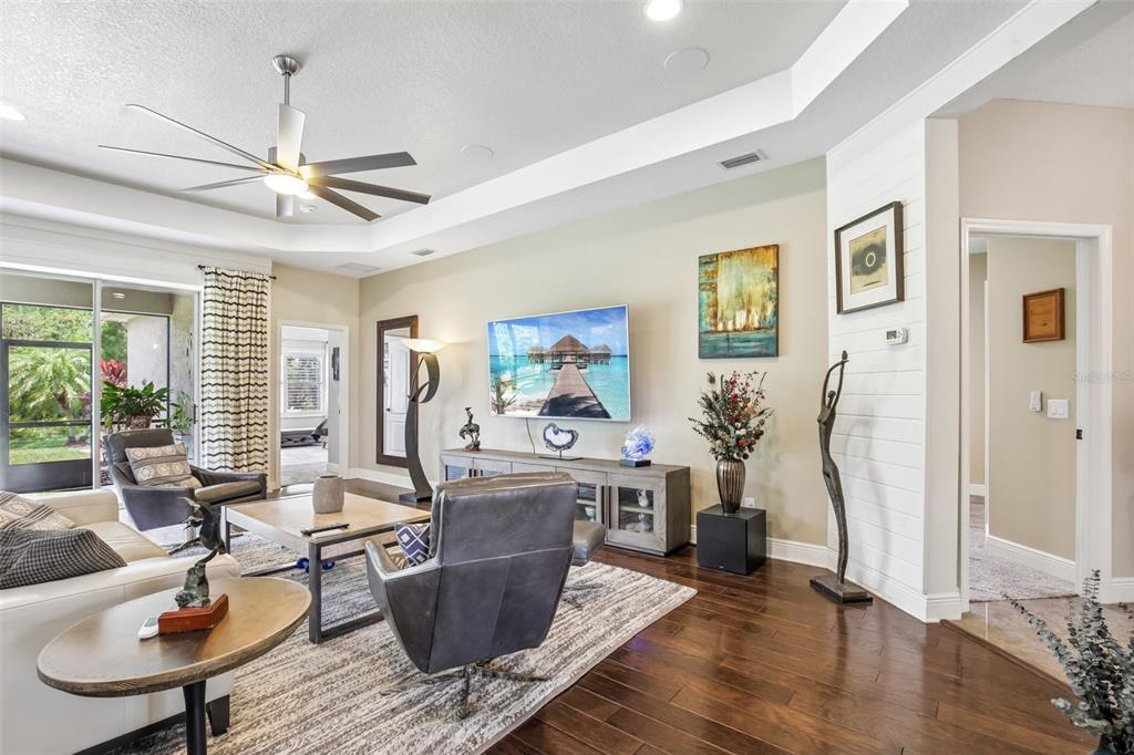 A living room features a tray ceiling, hardwood floors, a television, and a sliding glass door — 12307 WHISPER LAKE DRIVE, BRADENTON, FL