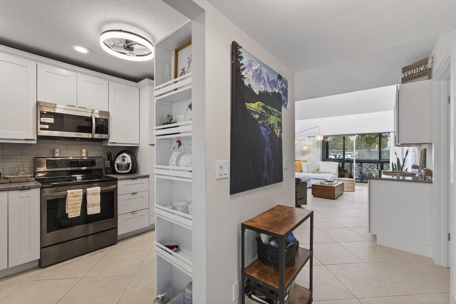 A kitchen with white cabinets and stainless steel appliances opens to a living area — 2532 S Boundbrook Dr S # 102, Palm Springs FL 33406, PALM SPRINGS, FL