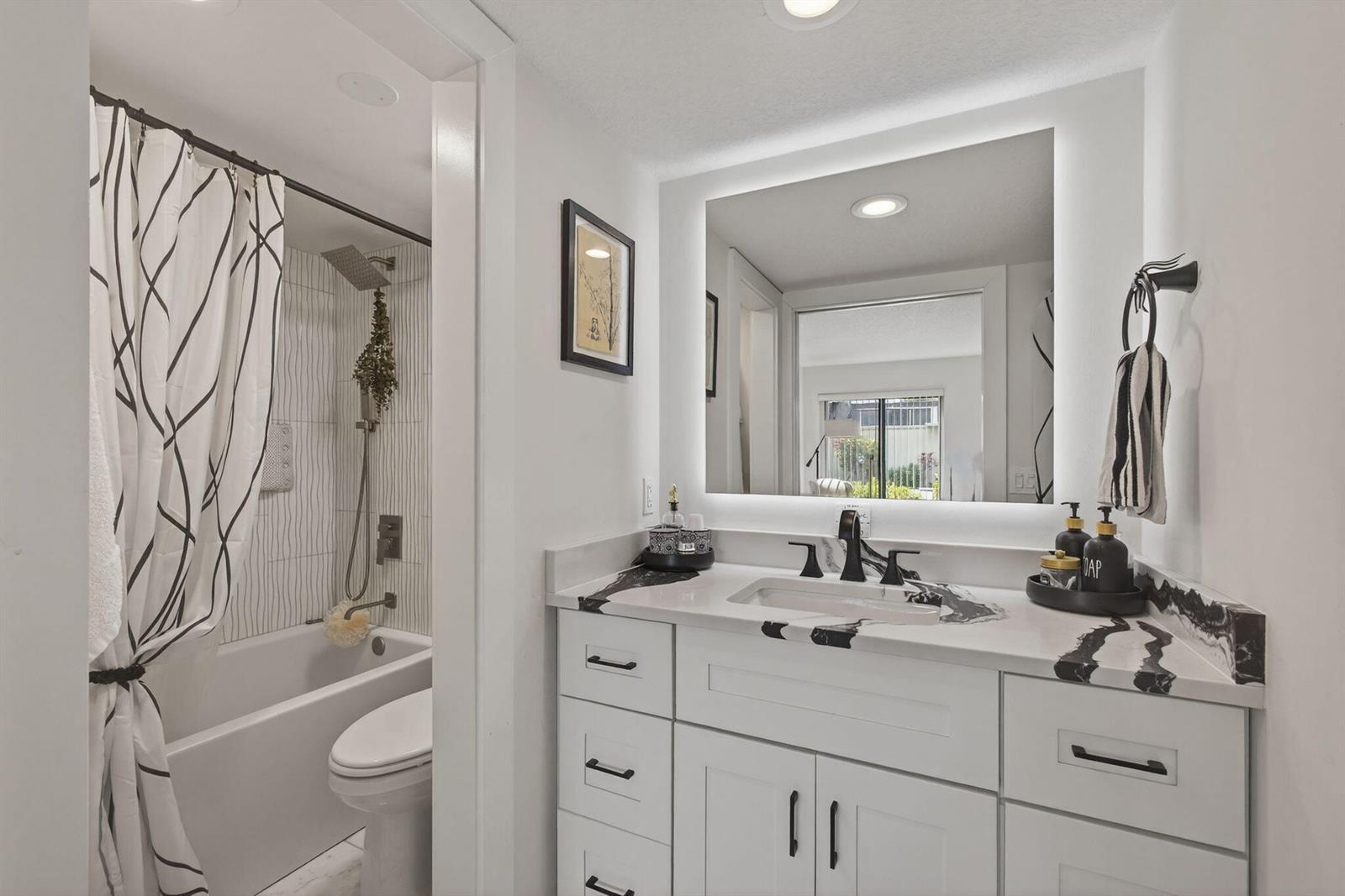A bathroom features a white vanity with a black and white marble countertop and mirror — 2532 S Boundbrook Dr S # 102, Palm Springs FL 33406, PALM SPRINGS, FL
