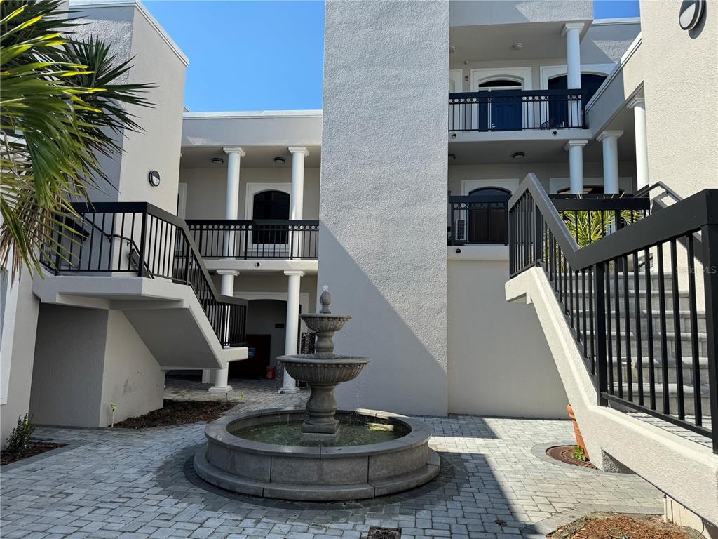 A stone fountain sits in a paved courtyard between two multi-story buildings with exterior staircases — 15434 N FLORIDA AVENUE, TAMPA, FL