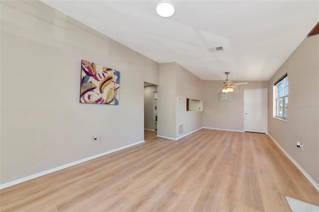 An empty living room features light wood-look flooring, beige walls, a ceiling fan, and a doorway — 3880 59TH AVENUE W UNIT 4196, BRADENTON, FL