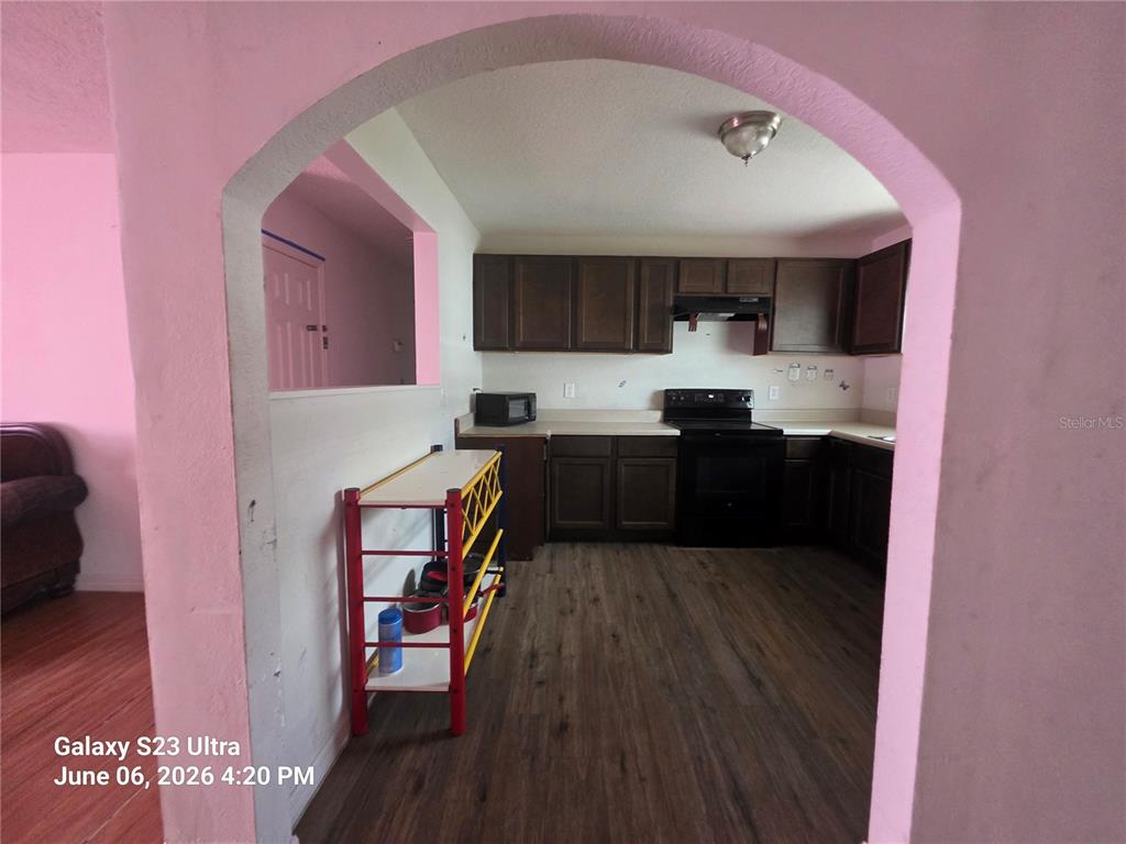 A kitchen with dark wood cabinets, black appliances, and wood-look flooring viewed through an archway — 2086 MARTIN LUTHER KING JR BOULEVARD, BARTOW, FL