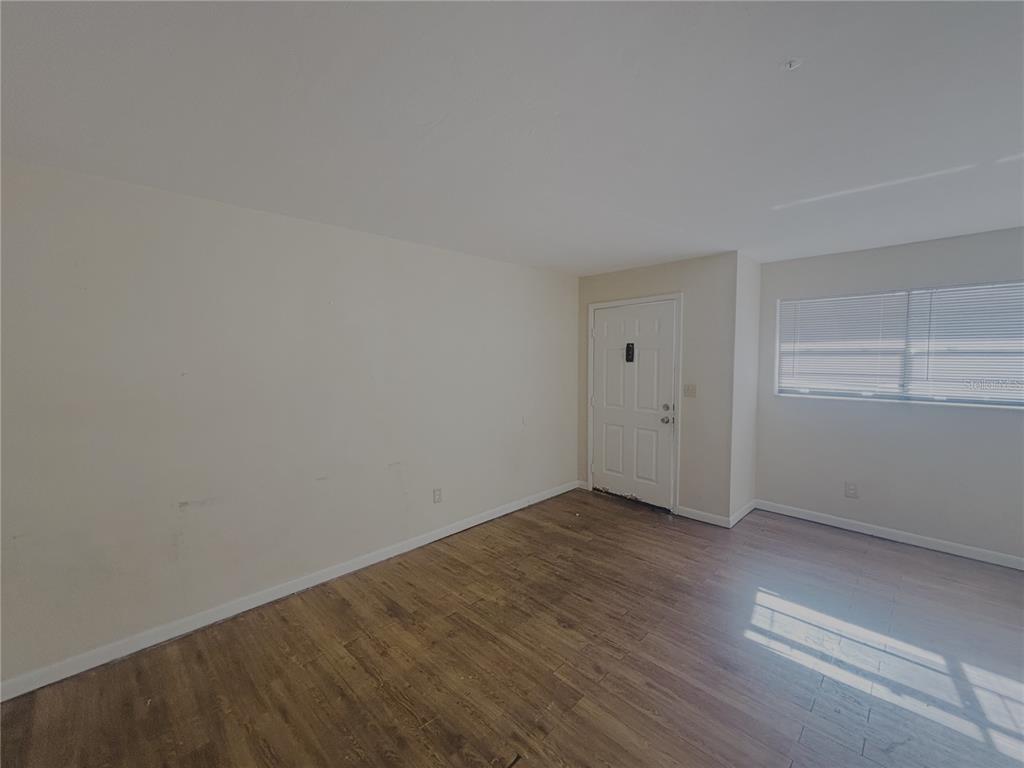 An empty room with light-colored walls, wood-look flooring, a white entry door, and a window — 1915 SW 70 TERRACE UNIT C, GAINESVILLE, FL