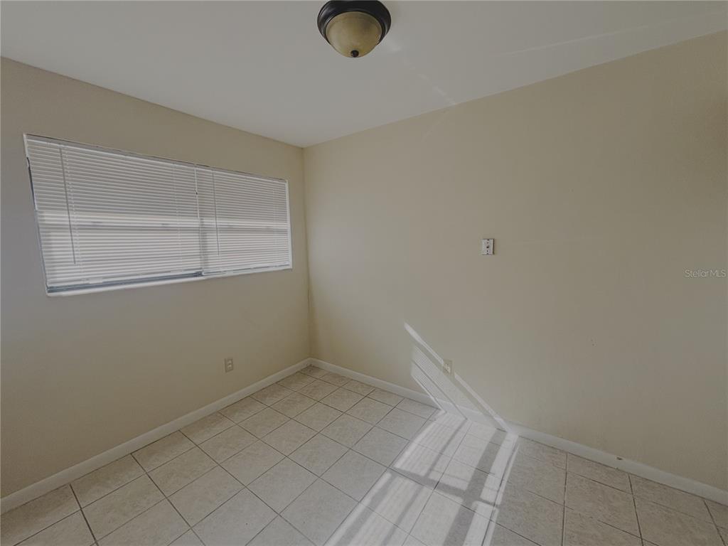 An empty room features beige walls, light-colored floor tiles, a window with blinds, and a ceiling light — 1915 SW 70 TERRACE UNIT C, GAINESVILLE, FL