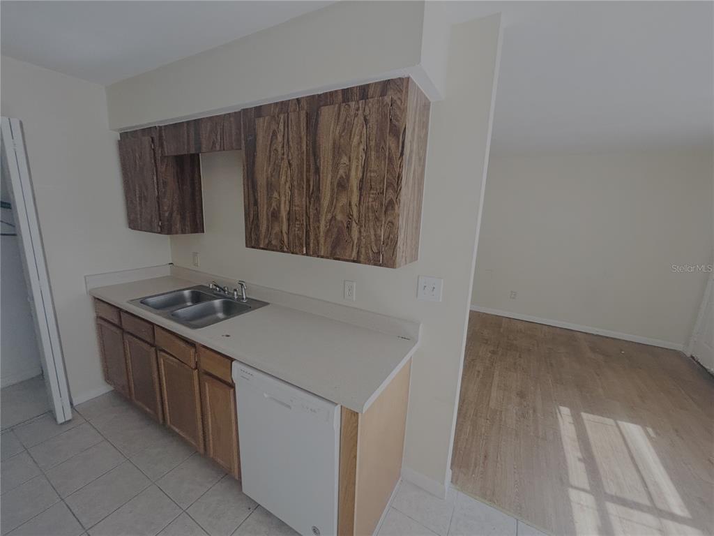 A kitchen features wood-grain cabinets, a double sink, a white dishwasher, and tiled flooring — 1915 SW 70 TERRACE UNIT C, GAINESVILLE, FL