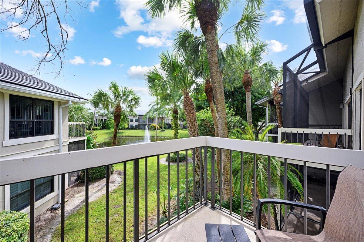 A balcony view overlooking a grassy lawn, palm trees, and a small pond with a fountain — 11863 Wimbledon Circle # 524, Wellington FL 33414, WELLINGTON, FL