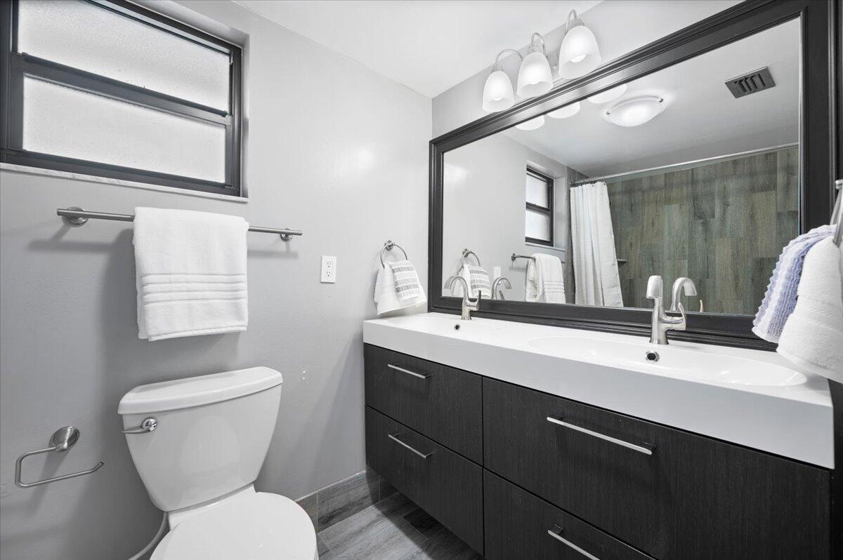 A modern bathroom features a dark wood double vanity, a large mirror, and gray walls — 11863 Wimbledon Circle # 524, Wellington FL 33414, WELLINGTON, FL