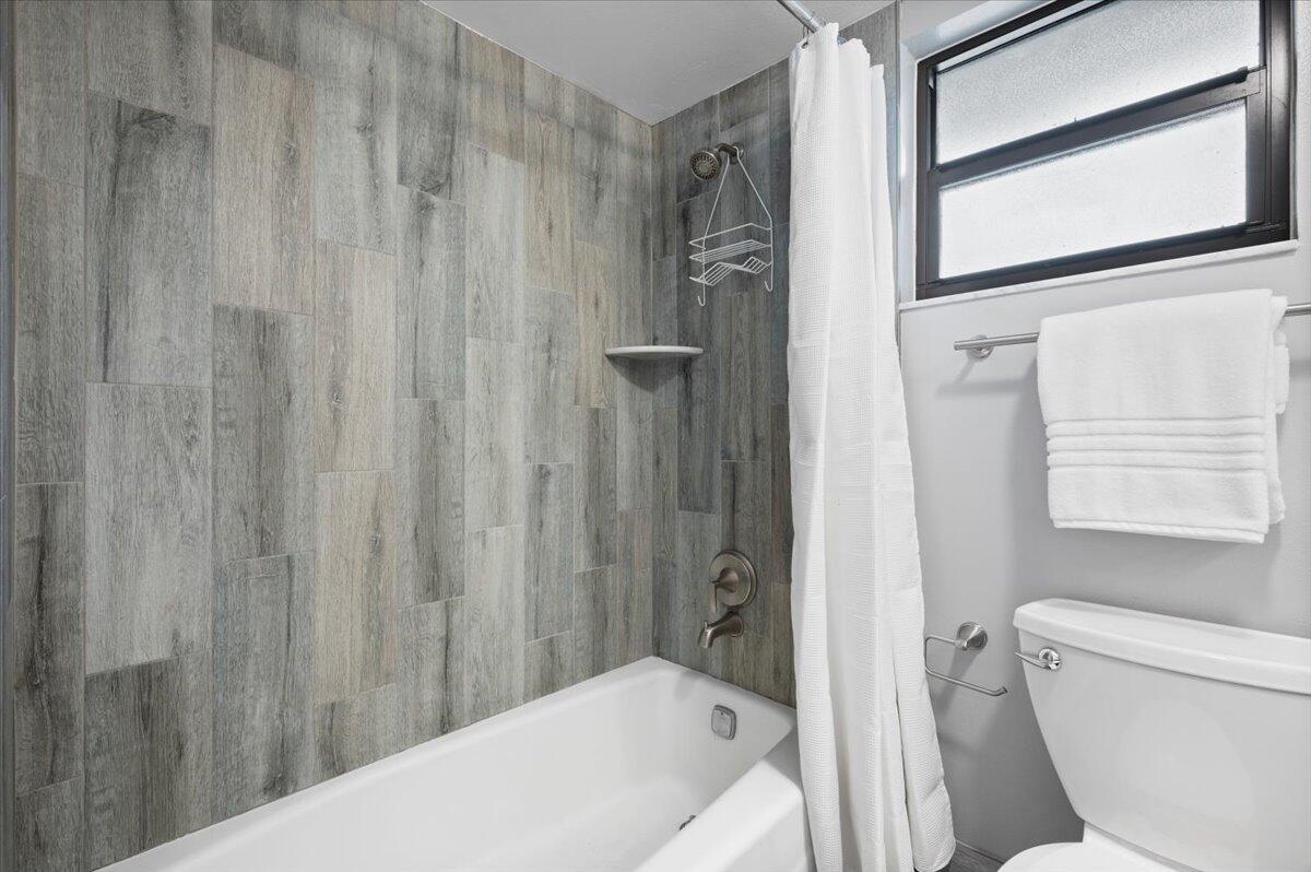 A bathroom features a bathtub with grey wood-look tile walls and a white shower curtain — 11863 Wimbledon Circle # 524, Wellington FL 33414, WELLINGTON, FL