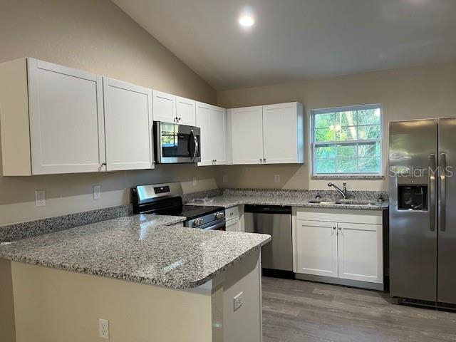 A kitchen features white cabinets, granite countertops, stainless steel appliances, and light wood flooring — 4366 SE 138TH STREET, SUMMERFIELD, FL