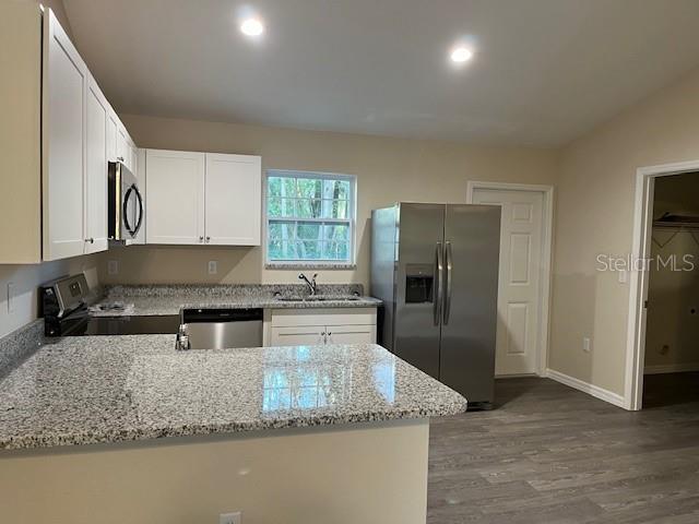 A kitchen features white cabinets, granite countertops, stainless steel appliances, and gray wood-look flooring — 4366 SE 138TH STREET, SUMMERFIELD, FL