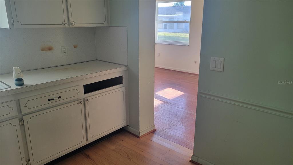 A kitchen with white cabinets and a countertop opens into a room with hardwood floors — 9850 LILY STREET N UNIT 117, PINELLAS PARK, FL