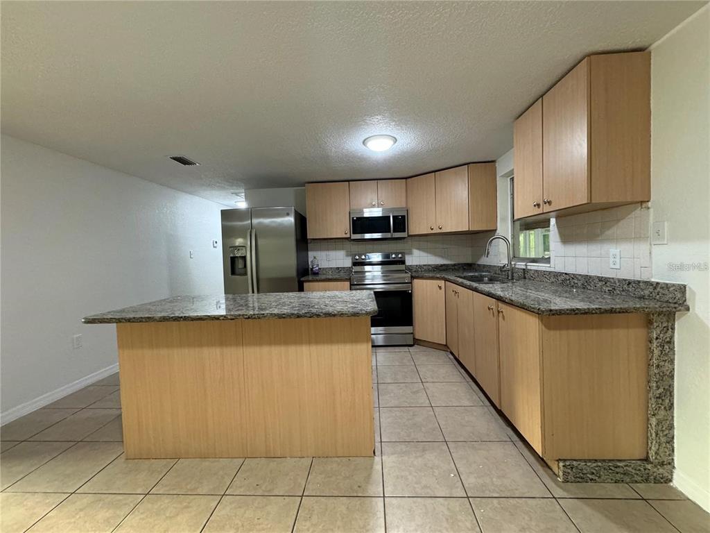 A kitchen features light wood cabinets, granite countertops, stainless steel appliances, and tile flooring — 10601 N 52ND STREET, TEMPLE TERRACE, FL