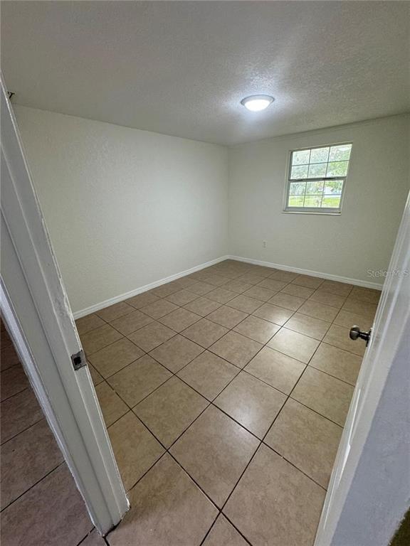 An empty room features beige tiled flooring, white walls, and a single window — 10601 N 52ND STREET, TEMPLE TERRACE, FL