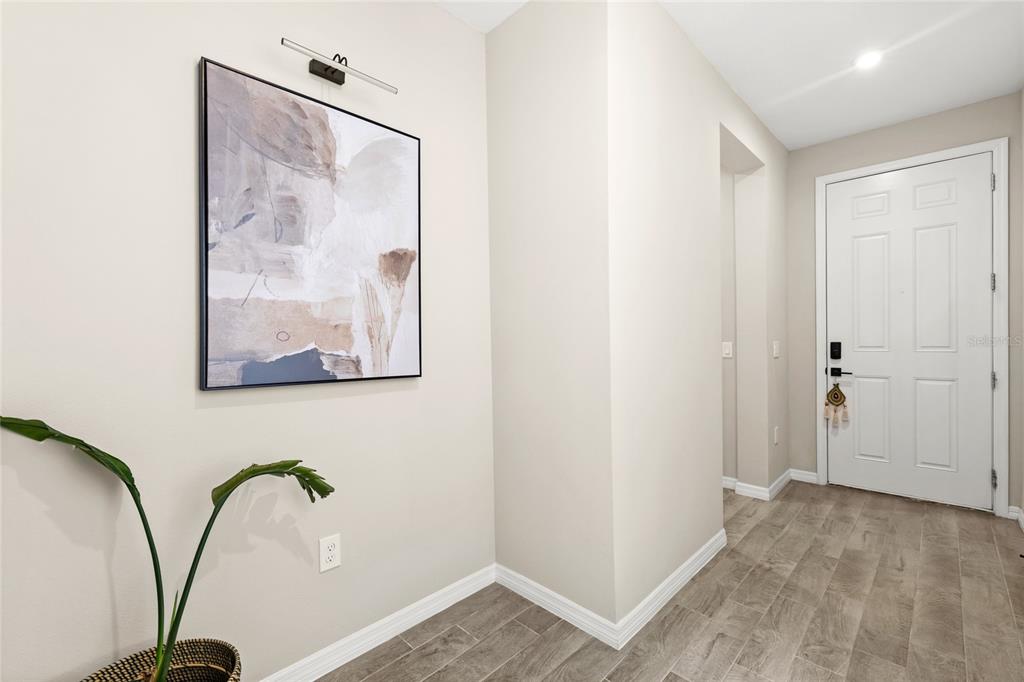 An entryway with light-colored walls, wood-look tile flooring, a framed abstract painting, and a white door — 1122 WILDMEADOW RUN, WINTER PARK, FL