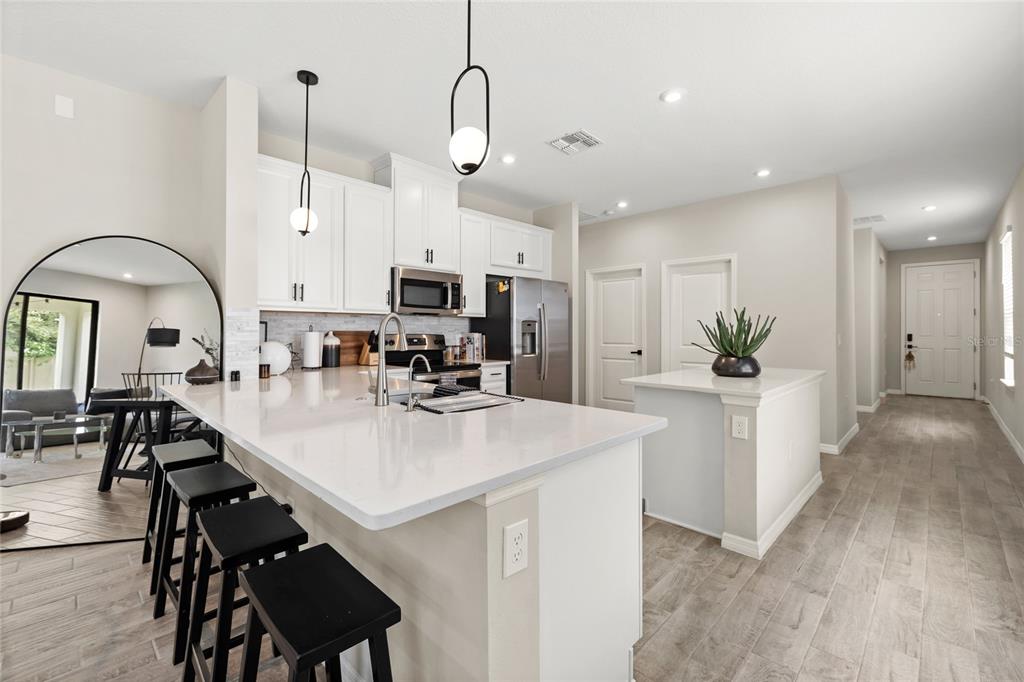 A modern kitchen features white cabinetry, quartz countertops, a center island, and black bar stools — 1122 WILDMEADOW RUN, WINTER PARK, FL