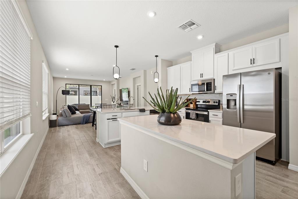 A kitchen with white cabinets, stainless steel appliances, and a quartz-topped island overlooks a living area — 1122 WILDMEADOW RUN, WINTER PARK, FL