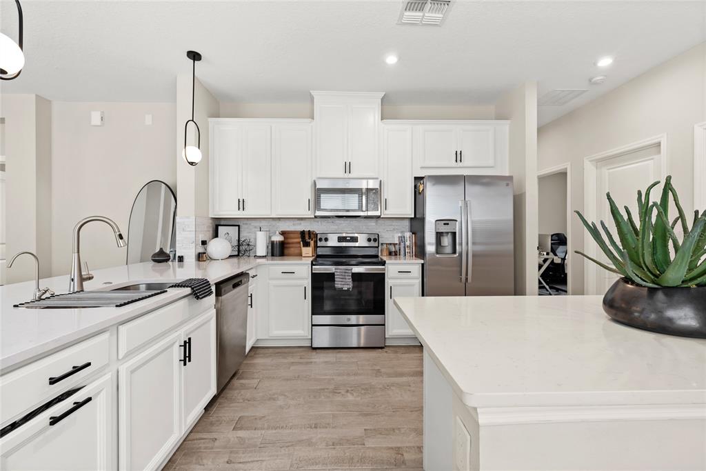 A modern kitchen features white cabinetry, stainless steel appliances, and a large quartz-topped island — 1122 WILDMEADOW RUN, WINTER PARK, FL