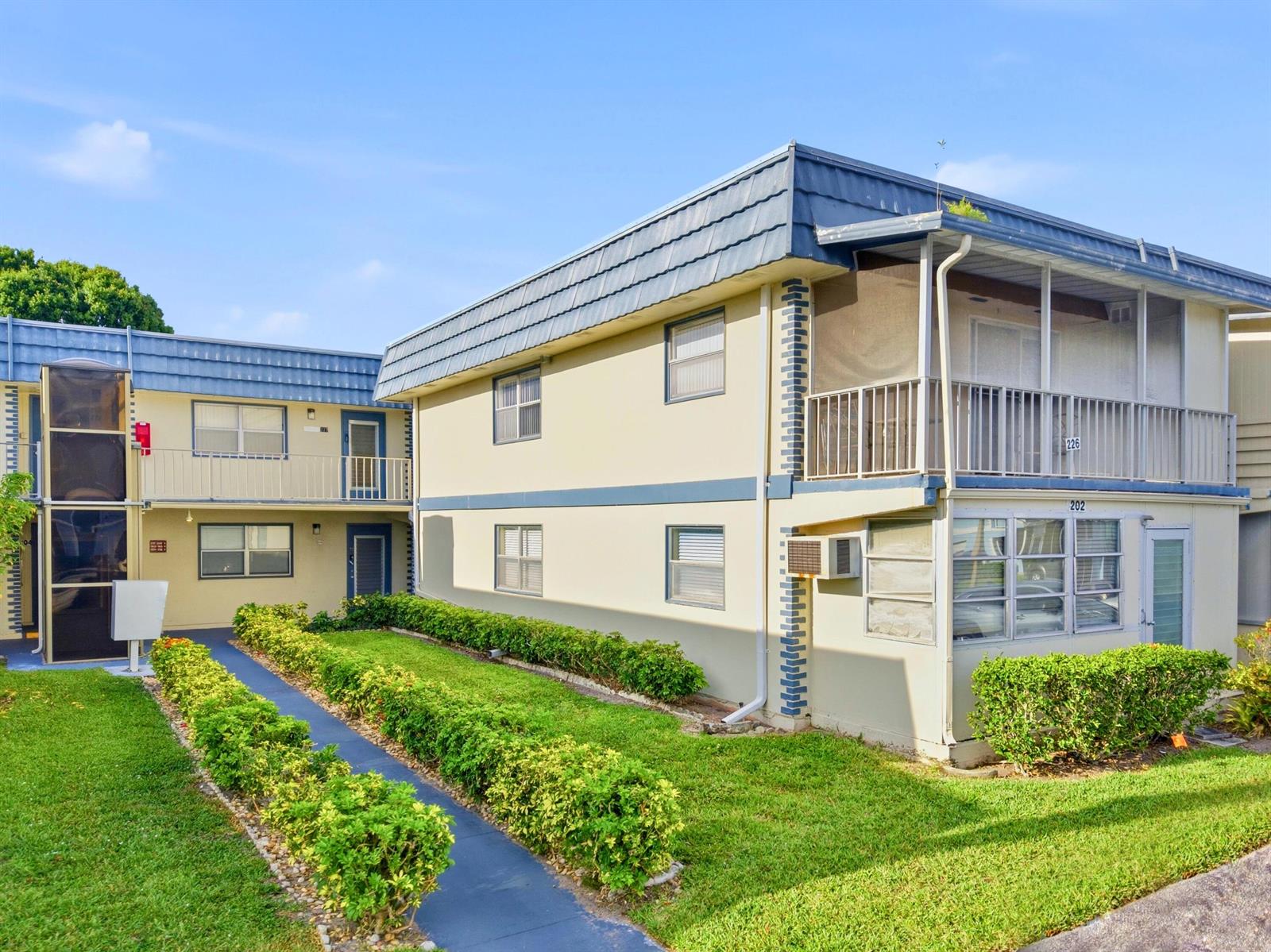 A two-story apartment building with a blue mansard roof and a landscaped walkway — 202 Brittany E, Delray Beach FL 33446, DELRAY BEACH, FL