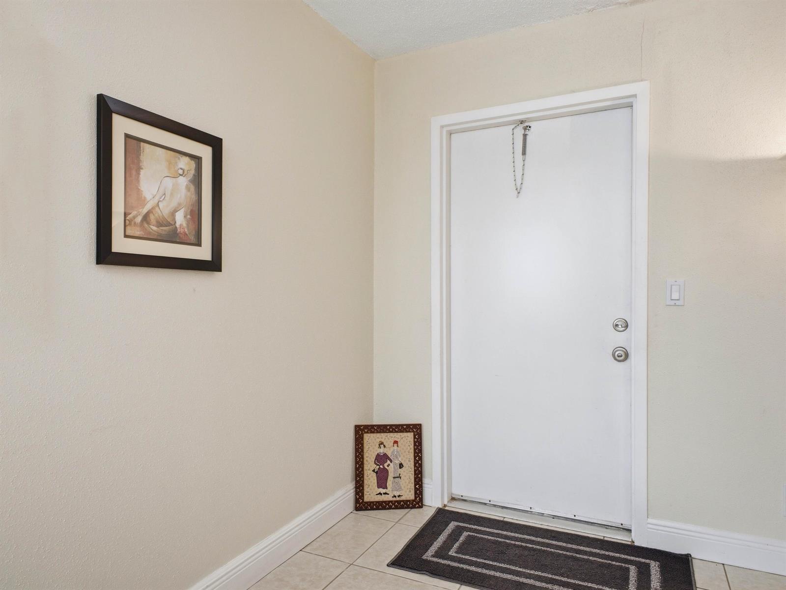 An entryway features a white door, tiled flooring, a wall-mounted picture, and a floor-level frame — 202 Brittany E, Delray Beach FL 33446, DELRAY BEACH, FL