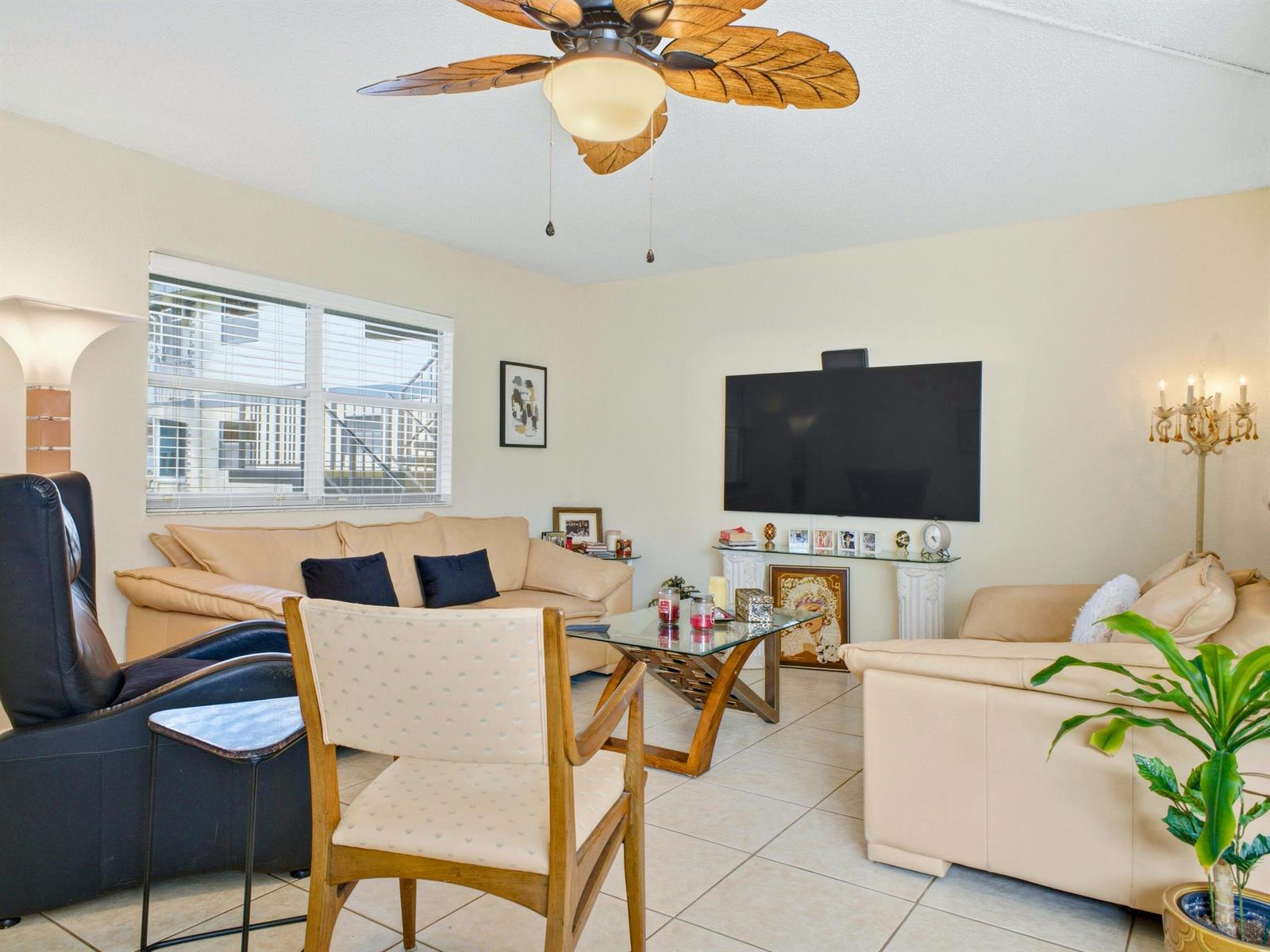 A living room features a ceiling fan, beige sofas, a glass coffee table, and a television — 202 Brittany E, Delray Beach FL 33446, DELRAY BEACH, FL