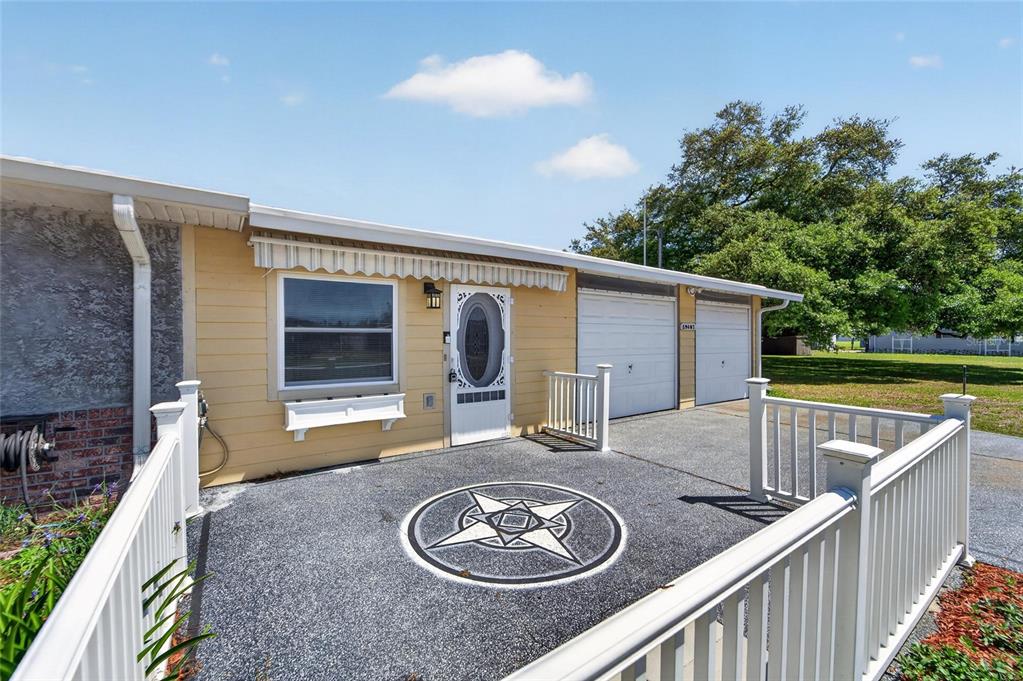 A yellow house exterior features a front patio with a star design and two garages — 39407 ROCKFORD AVENUE, ZEPHYRHILLS, FL