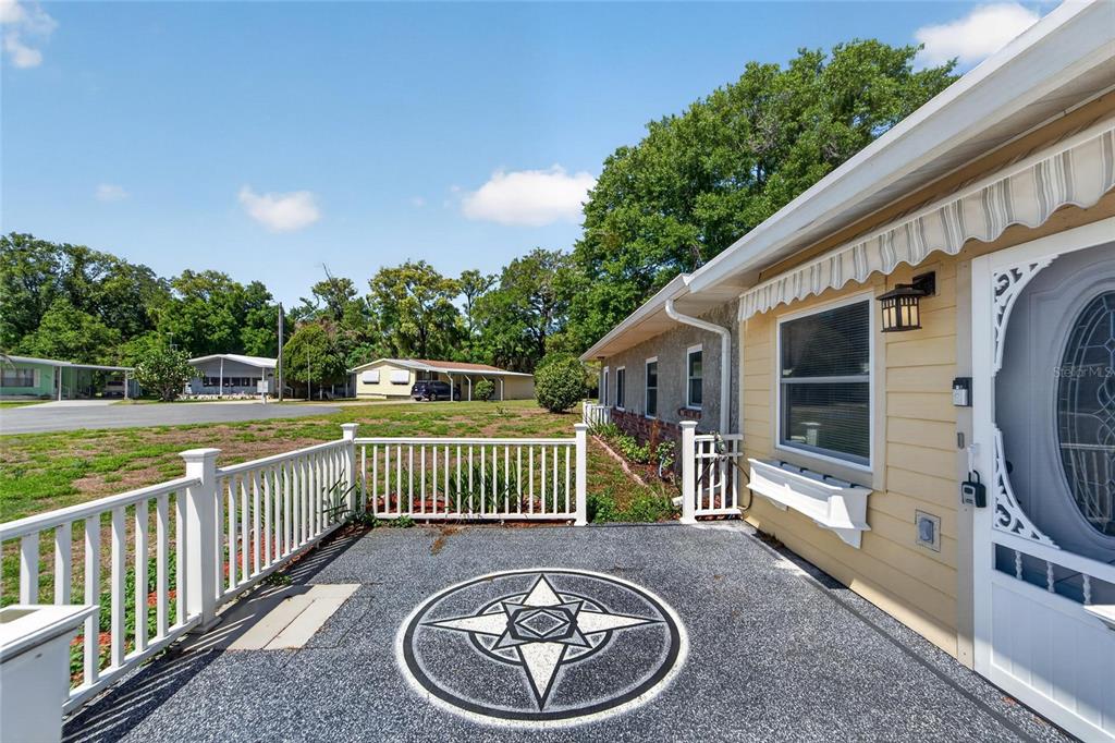 A paved patio with a star design sits beside a yellow house with white railings — 39407 ROCKFORD AVENUE, ZEPHYRHILLS, FL