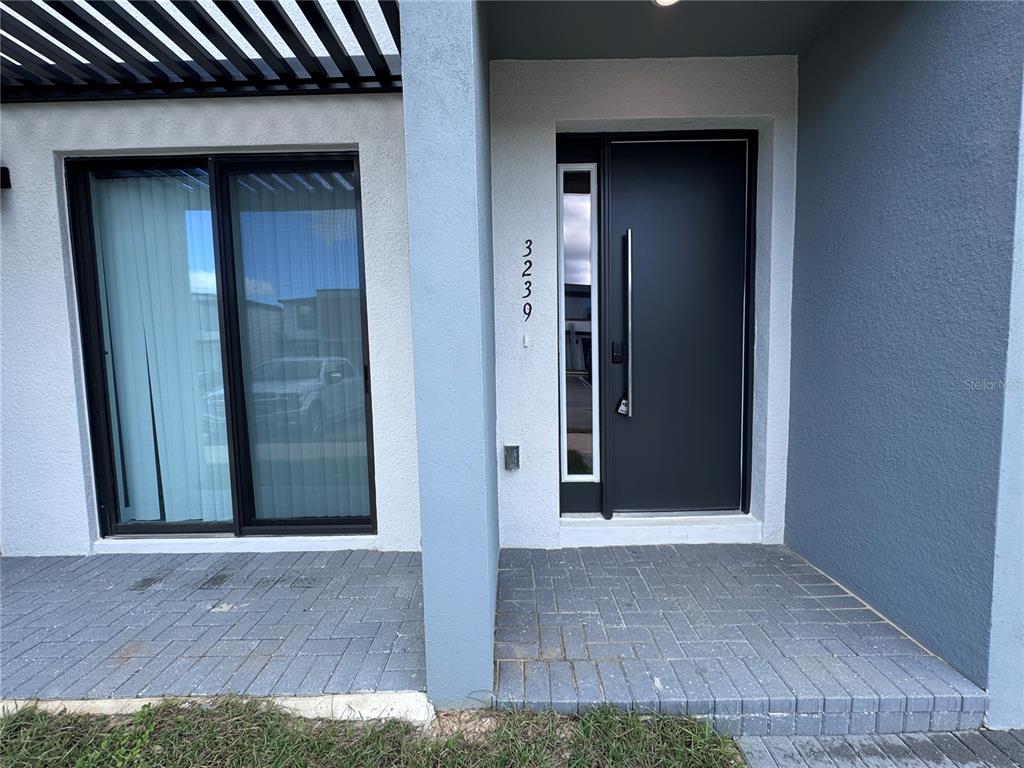 The exterior entrance features a dark gray front door, a sliding glass door, and pavers — 3239 SUSTAINABLE WAY, KISSIMMEE, FL