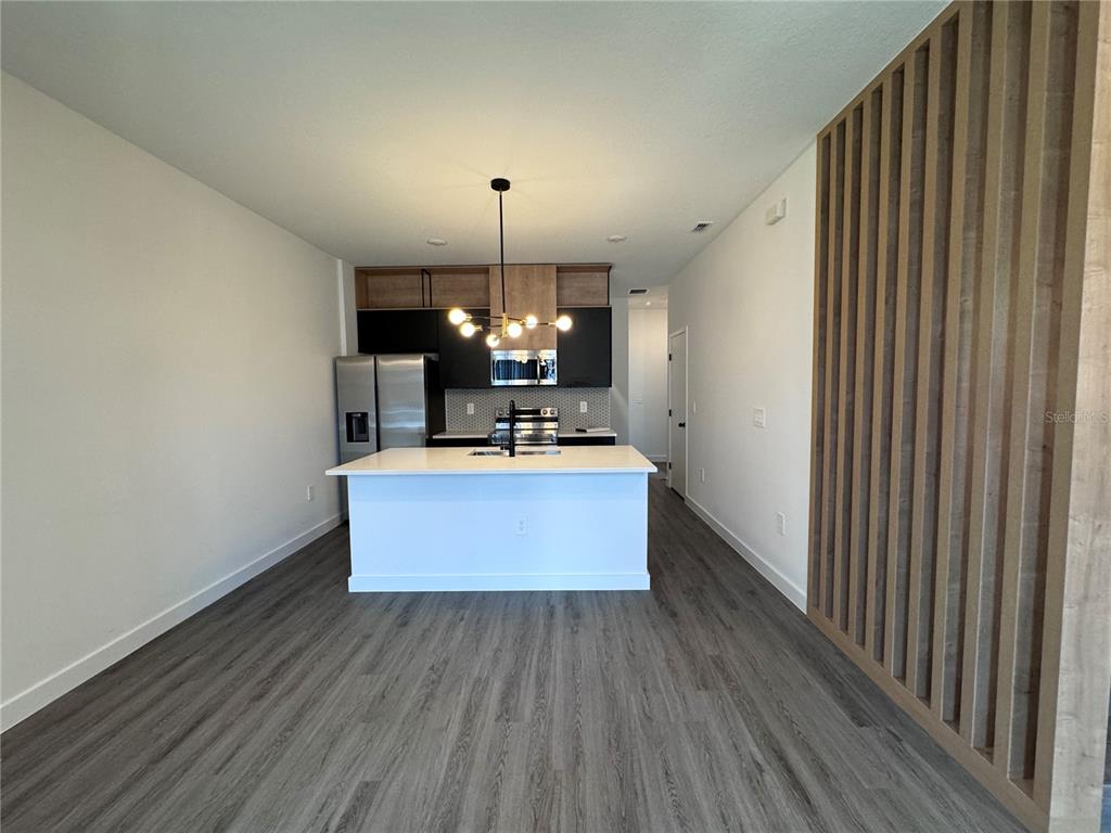 A modern kitchen features a white island, dark cabinetry, wood accents, and a contemporary chandelier — 3239 SUSTAINABLE WAY, KISSIMMEE, FL
