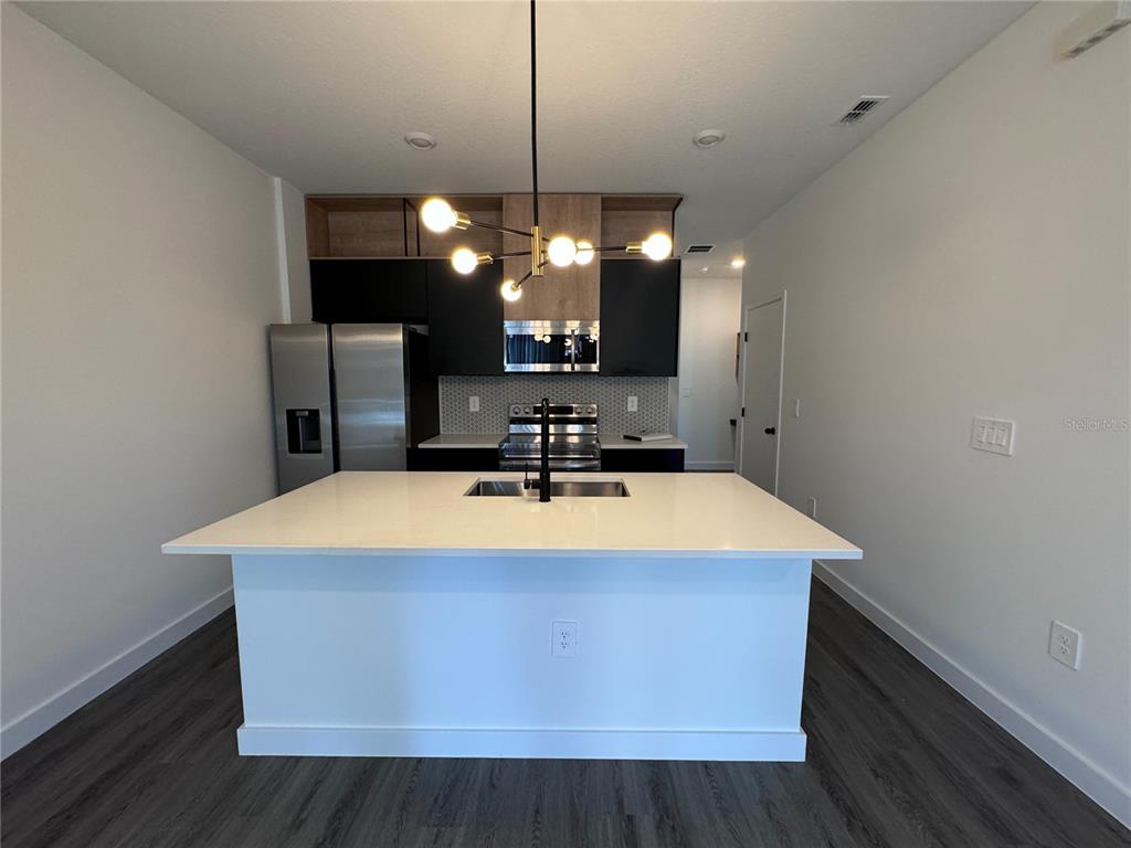 A modern kitchen features a white island, black cabinetry, stainless steel appliances, and a pendant light — 3239 SUSTAINABLE WAY, KISSIMMEE, FL