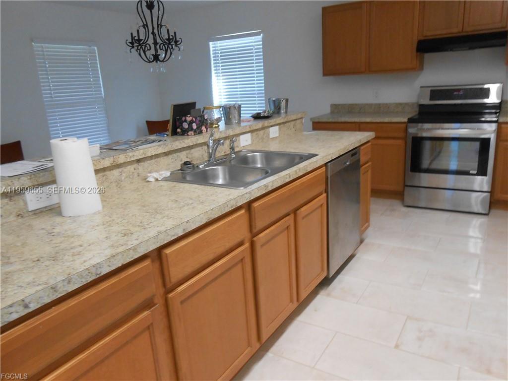 A kitchen features light-colored countertops, wooden cabinets, stainless steel appliances, and tile flooring — 154 Shadowview Ct., Lehigh Acres FL 33974, LEHIGH ACRES, FL