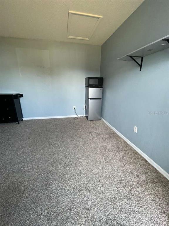 A room with gray walls, gray carpeting, a small refrigerator, and a wall-mounted shelf — 241 CARIBBEAN DRIVE Front Unit, DAVENPORT, FL