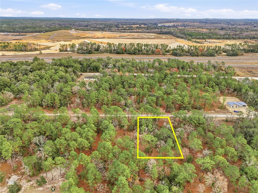 An aerial view shows a wooded lot outlined in yellow near a highway — CAYMAN ROAD, WEEKI WACHEE, FL