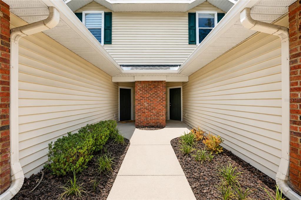 A concrete walkway leads to two dark front doors flanked by beige siding and brick — 13200 W NEWBERRY ROAD UNIT 199, NEWBERRY, FL