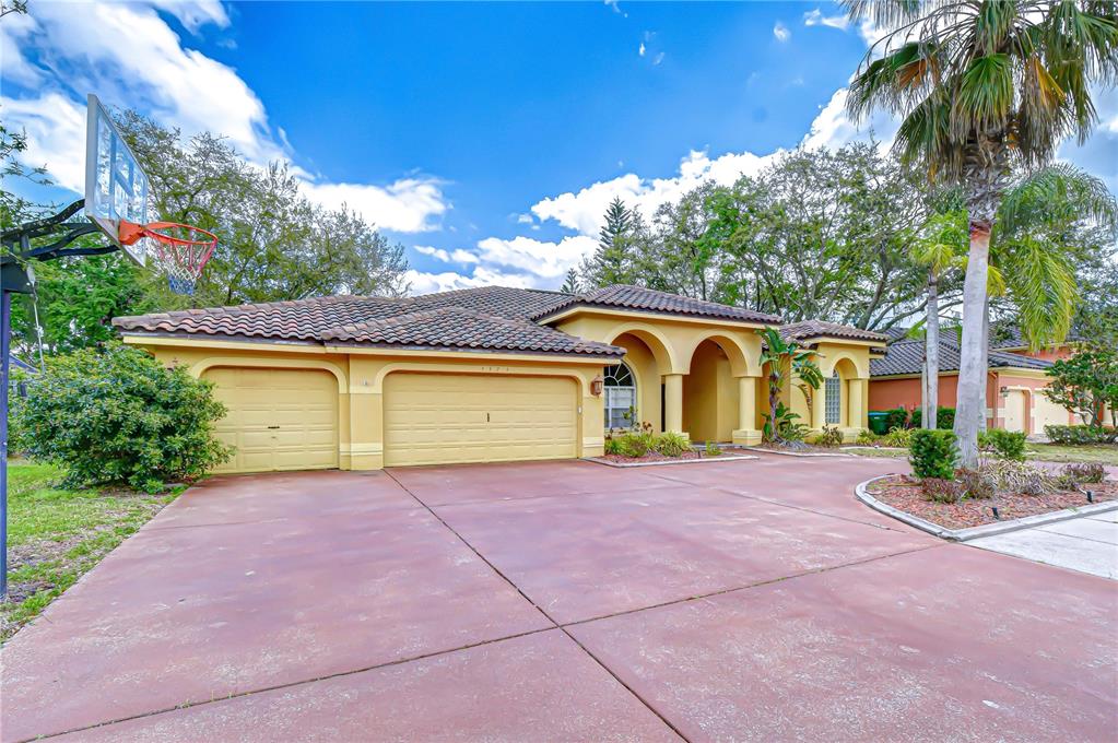 A yellow single-story house with a tile roof, three-car garage, and a basketball hoop — 3373 CRESCENT OAKS BOULEVARD, TARPON SPRINGS, FL