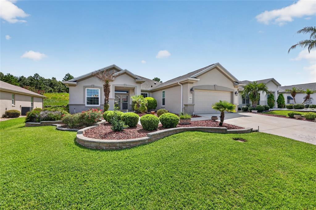 A single-story house with a beige stucco exterior, a two-car garage, and landscaped front yard — 9785 SE 125TH LANE, SUMMERFIELD, FL