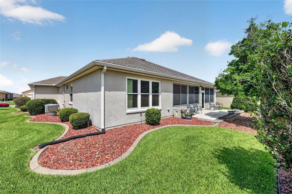 The exterior of a beige house features a screened-in patio, red landscaping rocks, and lawn — 9785 SE 125TH LANE, SUMMERFIELD, FL