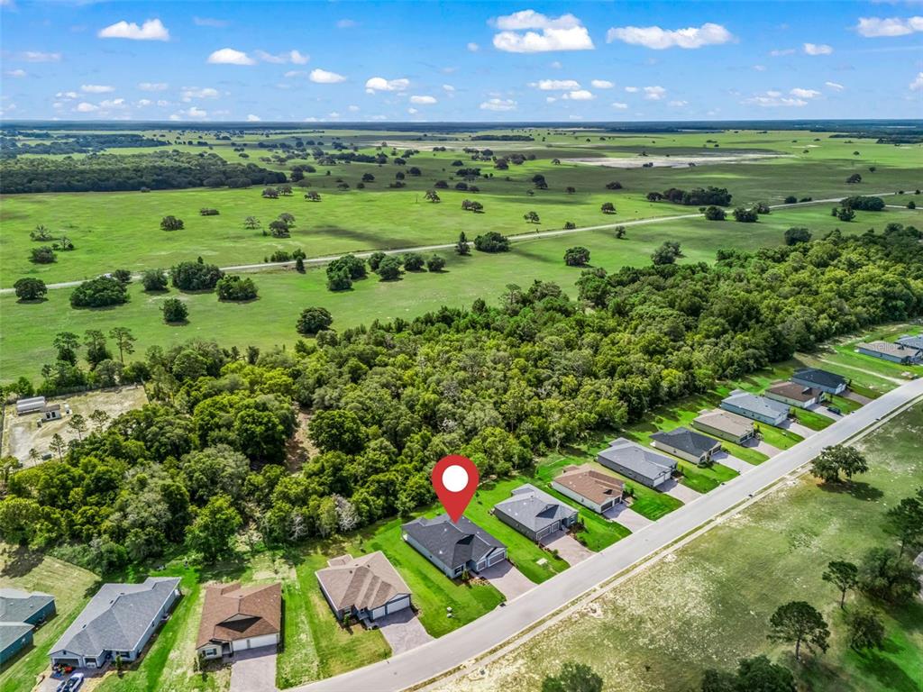An aerial view shows a suburban street with houses bordering a large, wooded field — 6510 SW 180TH CIRCLE, DUNNELLON, FL