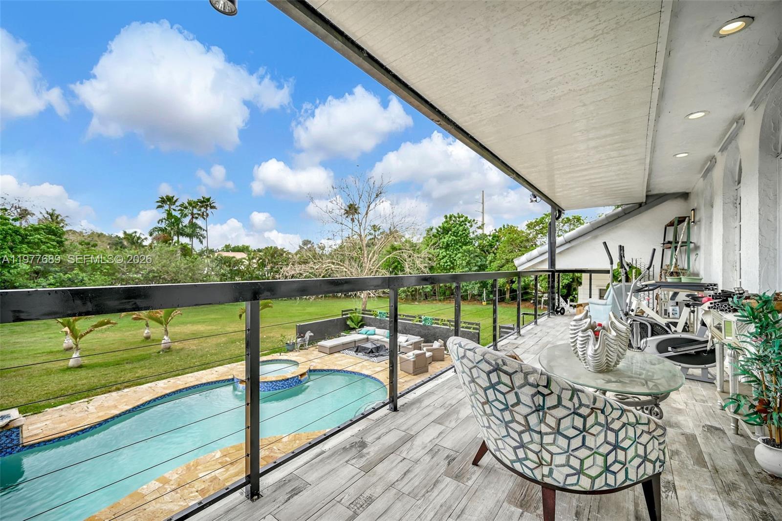 A modern kitchen features a large stone island, transparent bar stools, and a wooden staircase — 18950 SW 50th St, Southwest Ranches FL 33332, SOUTHWEST RANCHES, FL
