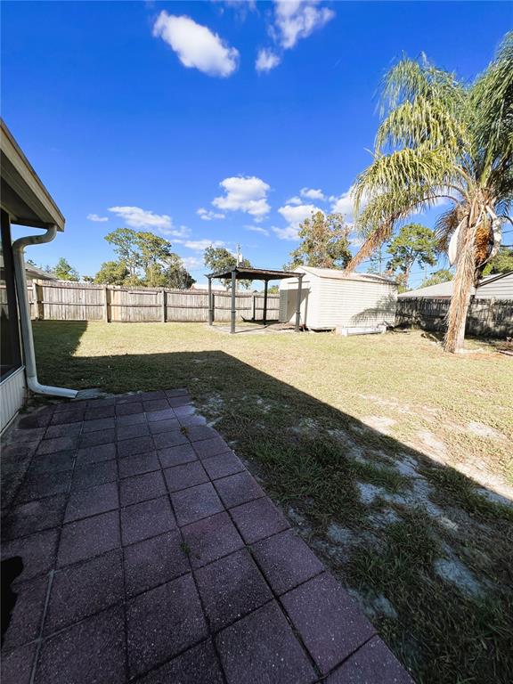 A backyard features a paved patio, a wooden fence, a shed, and a palm tree — 1706 HOWLAND BOULEVARD, DELTONA, FL