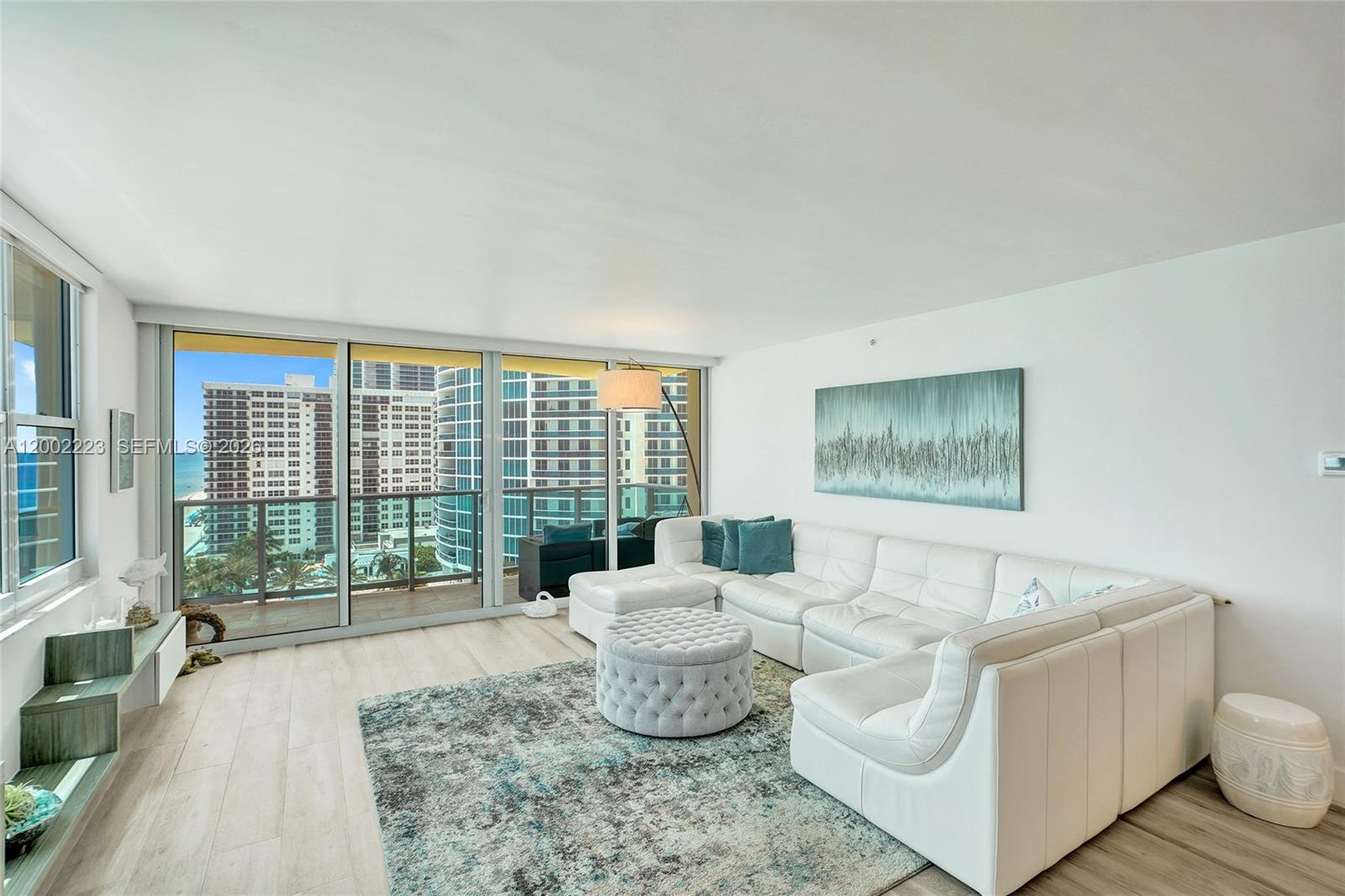 A living room features a white sectional sofa, a tufted ottoman, and floor-to-ceiling balcony windows — 2501 S Ocean Dr # 1211, Hollywood FL 33019, HOLLYWOOD, FL