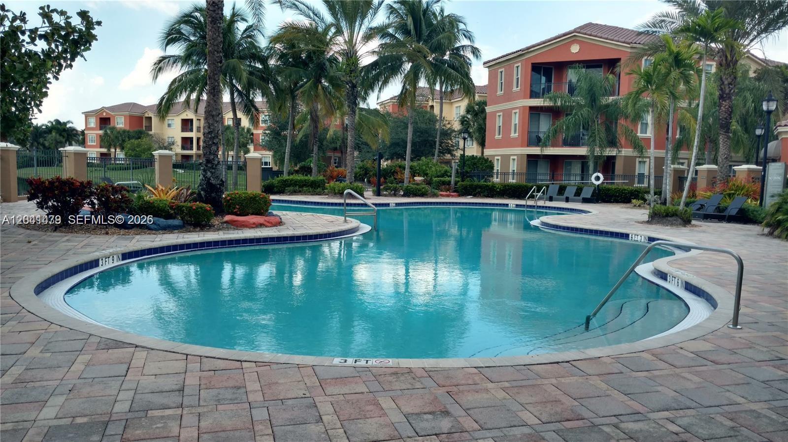 A swimming pool with depth markers is surrounded by a paved deck and palm trees — 4506 SW 160th Ave # 1116, Miramar FL 33027, MIRAMAR, FL