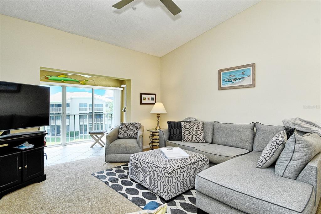 A living room features a gray sectional sofa, patterned ottoman, television, and sliding glass doors — 9610 CLUB SOUTH CIRCLE UNIT 4302, SARASOTA, FL