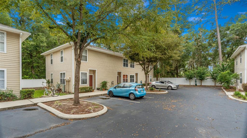 A two-story apartment building with tan siding and a parking lot in the foreground — 1710 NW 7TH STREET UNIT 303, GAINESVILLE, FL