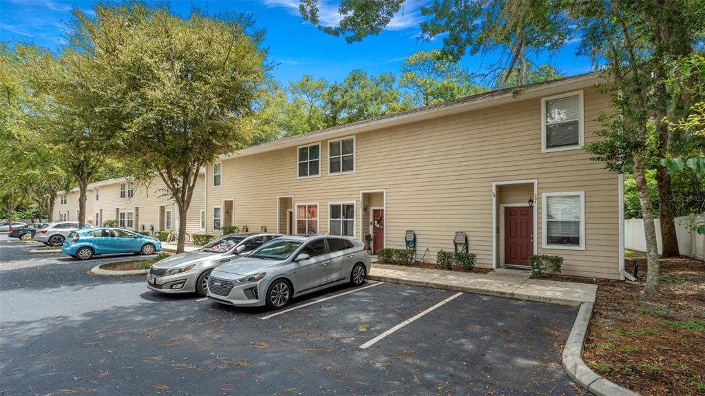 A two-story tan townhouse with a parking lot in front and several parked cars — 1710 NW 7TH STREET UNIT 303, GAINESVILLE, FL