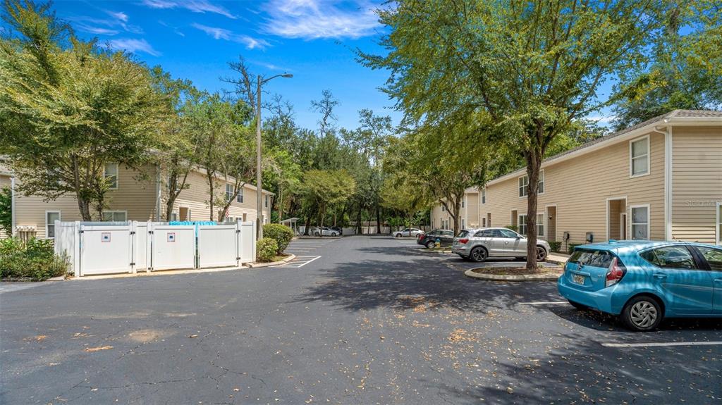 A parking lot sits between two rows of beige two-story apartment buildings with trees — 1710 NW 7TH STREET UNIT 303, GAINESVILLE, FL