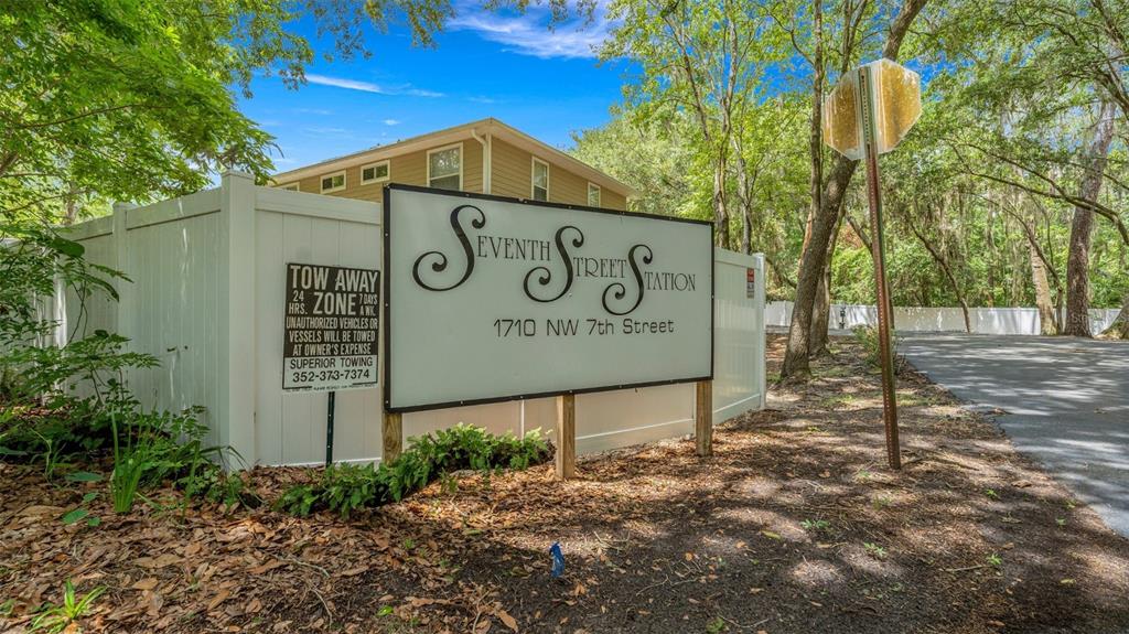 A sign for Seventh Street Station stands in front of a white fence and trees — 1710 NW 7TH STREET UNIT 303, GAINESVILLE, FL