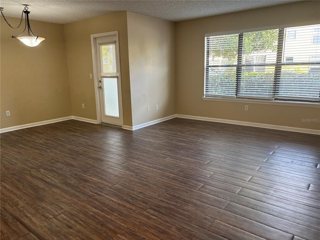 An empty room features wood-look flooring, beige walls, a glass-paneled door, and large windows — 11901 4TH STREET N UNIT 7107, ST PETERSBURG, FL