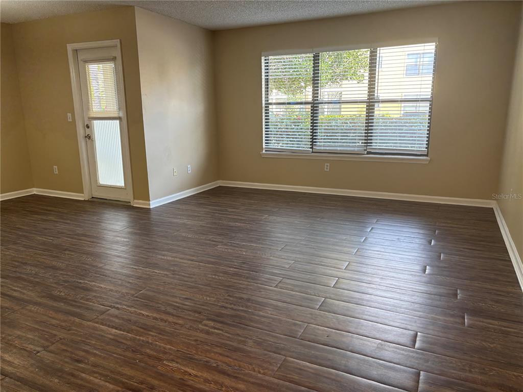 An empty room features dark wood-look flooring, beige walls, a glass-paneled door, and large windows — 11901 4TH STREET N UNIT 7107, ST PETERSBURG, FL