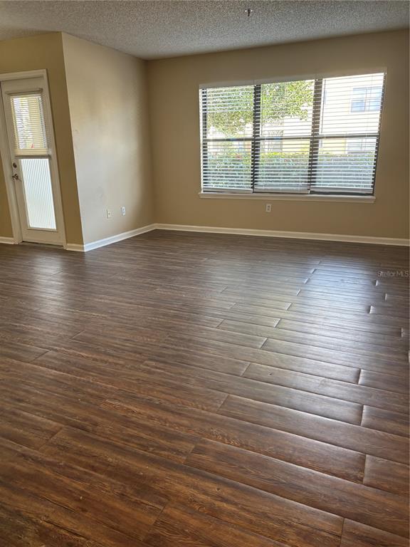 An empty room with wood-look flooring, a glass-paneled door, and a large window with blinds — 11901 4TH STREET N UNIT 7107, ST PETERSBURG, FL