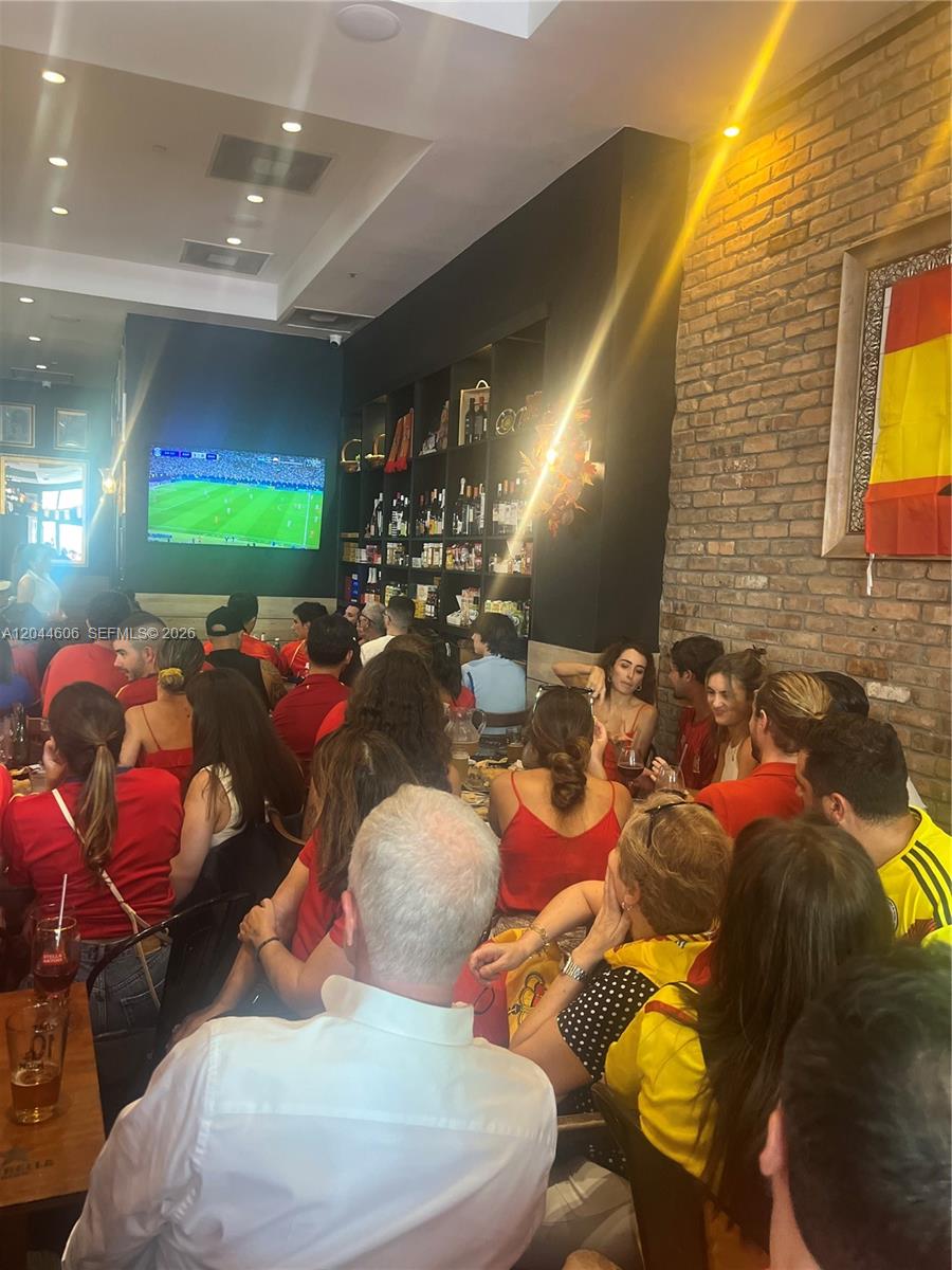 A crowded restaurant interior features a large television screen, a brick wall, and bar shelving — 3252 NE 1ST AVE, Miami FL 33137, MIAMI, FL